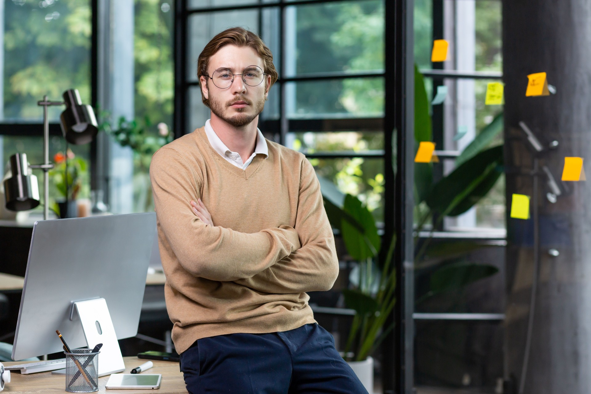 A young man freelancer, programmer, designer in the office, crosses his arms, , looks into the camera